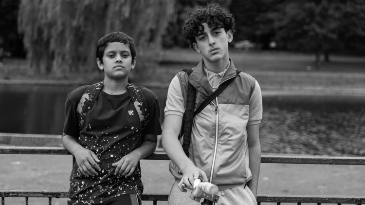 A black and white photo of two teenage boys leaning against a railing looking at the camera.