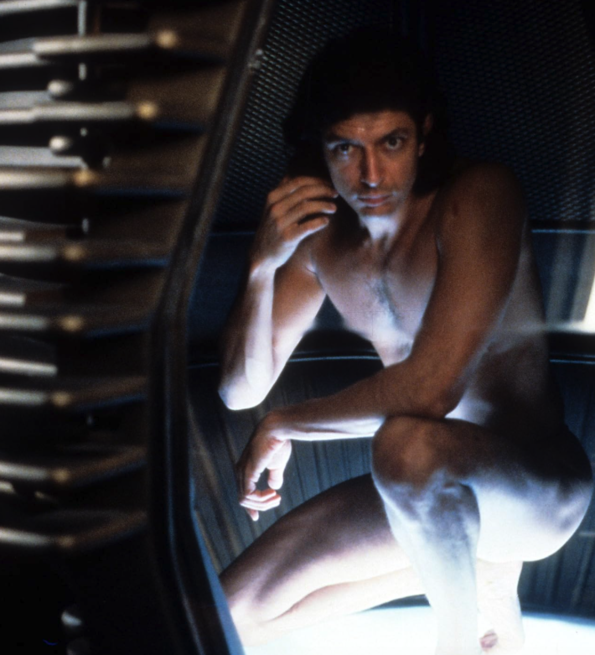 Shirtless man crouches inside a dark futuristic chamber, lit by glowing steps and a bright floor.