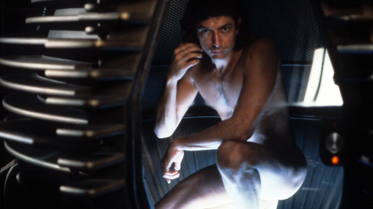 Shirtless man crouches inside a dark futuristic chamber, lit by glowing steps and a bright floor.