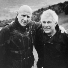 A black and white photo of two men standing outside with their arms around each other.