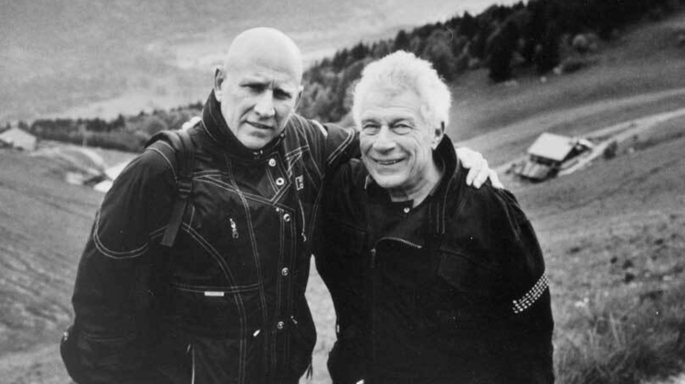 A black and white photo of two men standing outside with their arms around each other.