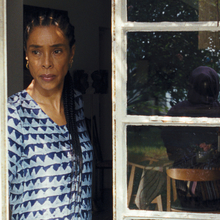 A woman standing by an open window looking out.