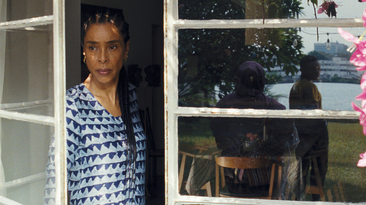 A woman standing by an open window looking out.
