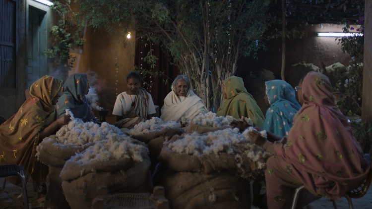 A group of women sitting around bags of cotton.