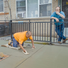 A man laying concrete while another man looks on.