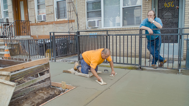 A man laying concrete while another man looks on.