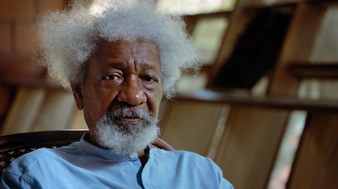 Close-up portrait of an older man with white hair and beard, wearing a blue shirt and looking at the camera.