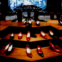 Rows of red, black, and white high-heeled shoes displayed on wooden platforms in a dimly lit setting.