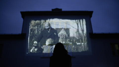 Silhouetted viewer watches a black-and-white film projected on a large screen in a dark theatre.