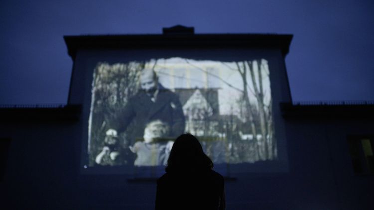 Silhouetted viewer watches a black-and-white film projected on a large screen in a dark theatre.