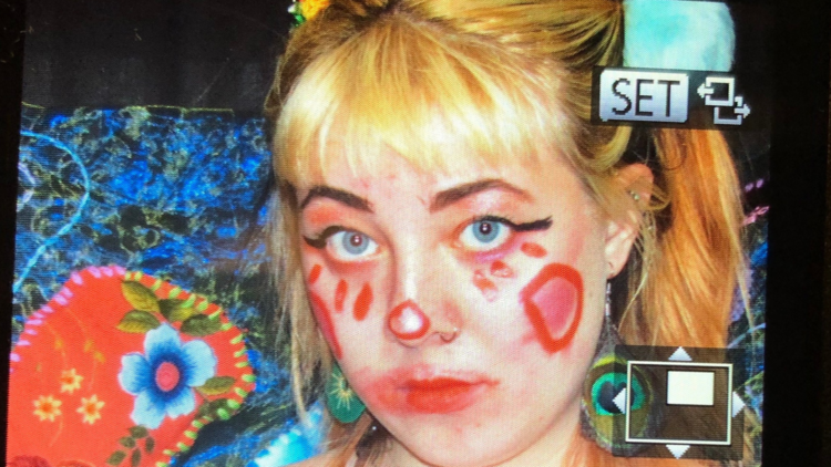 An image of the Raina Griefer a white artist with blonde hair and clown makeup on rendered in a 90's VHS style.