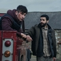 Barry Keoghan looks off into the distance sitting in the back of a red van, whilst Christopher Abott looks in his direction whilst leaning on the red van.