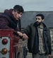 Barry Keoghan looks off into the distance sitting in the back of a red van, whilst Christopher Abott looks in his direction whilst leaning on the red van.