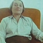 A lady sits in a chair and looks off into the distance.