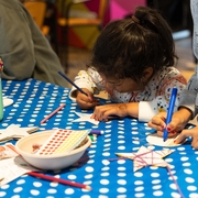 A young girl colours in a star with a blue pencil ontop of a spotty blue table cloth.