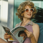 A still from the film Far From Heaven. A woman in a purple dress sits on a lounge chair, reading a Cosmopolitan magazine.