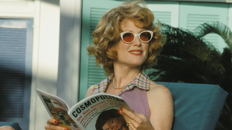 A still from the film Far From Heaven. A woman in a purple dress sits on a lounge chair, reading a Cosmopolitan magazine.