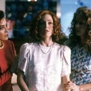 Three women in colorful outfits pose closely together, showcasing vintage 1990s fashion, with textured hairstyles and pearls.