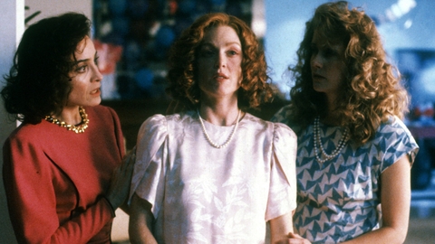 Three women in colorful outfits pose closely together, showcasing vintage 1990s fashion, with textured hairstyles and pearls.
