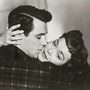 A close embrace between two people, showcasing intimacy with hands gently touching, set against a soft-focus background.