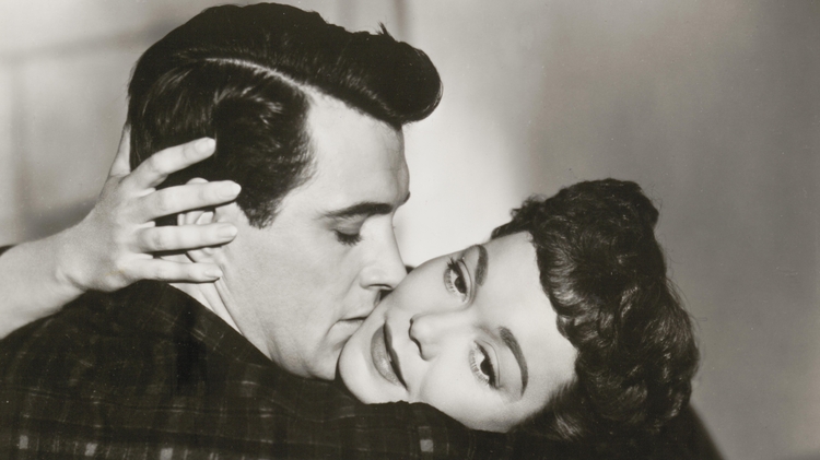 A close embrace between two people, showcasing intimacy with hands gently touching, set against a soft-focus background.