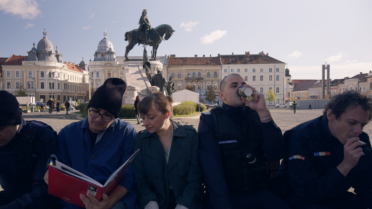 A still from the film Kontinental '25 - five people sit on a bench, two of them looking at a book, while the others are drinking and smoking.