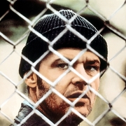 A man wearing a black beanie is partially seen behind a chain link fence.