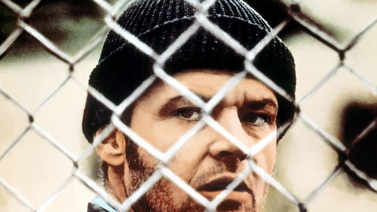A man wearing a black beanie is partially seen behind a chain link fence.