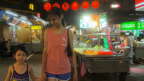 A still from the film Left-Handed Girl showing a woman and child walking through a night market in Taipei holding hands.