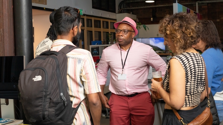 A group of people standing around chatting in the Pervasive Media Studio.