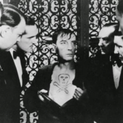 An gathering of elegantly dressed individuals, against an ornate ironwork background.