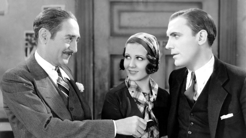 Three elegantly dressed individuals engage in conversation, with one holding a small object in their hand against a vintage backdrop.