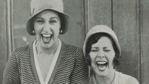 Two women holding hands laughing out loud.