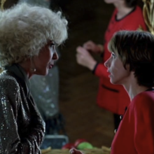 Two women engage in conversation in front of a vintage mirror, accentuated by elegant lighting and retro-style decor.