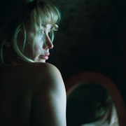 A woman with wavy hair is captured from behind, softly illuminated against a dark background.