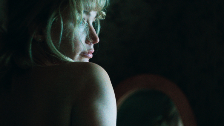 A woman with wavy hair is captured from behind, softly illuminated against a dark background.