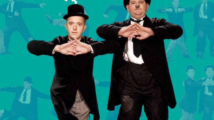 Two men in classic bowler hats and tuxedos perform a comedic pose against a vibrant teal backdrop, promoting a slapstick event.
