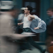 A man in a white tank top runs through a busy street, papers flying around him, creating a sense of urgency and motion.