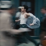 A man in a white tank top runs through a busy street, papers flying around him, creating a sense of urgency and motion.