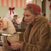Two women in vintage holiday attire converse in a festive store, surrounded by Christmas decorations and shoppers.
