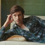 A person in a plaid shirt lounges on a couch, resting their head on one hand against a green wall.