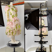 An image in three parts - in the left image, a mannequin with a dress on, stood on a pedestal; the dress is a sheer adjacent material, is shell pink in colour, and has green flowers dotted all over it. In the middle, the mannequin sits at the centre of a photography studio, with digital photography equipment surrounding it, to capture a render, shown in the image on the far right. 