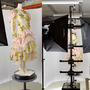 An image in three parts - in the left image, a mannequin with a dress on, stood on a pedestal; the dress is a sheer adjacent material, is shell pink in colour, and has green flowers dotted all over it. In the middle, the mannequin sits at the centre of a photography studio, with digital photography equipment surrounding it, to capture a render, shown in the image on the far right. 