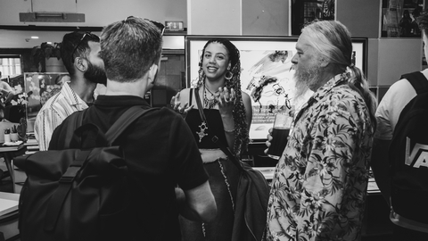 A group of diverse people are engaging in lively conversation in an indoor setting. The atmosphere is casual and friendly, with one person smiling as they speak.