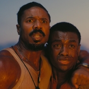 Two men embrace each other, showcasing a strong bond, under a warm sunset.