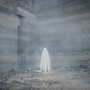A ghostly figure in a white sheet stands amid a foggy, industrial construction site, with concrete walls and scattered debris.