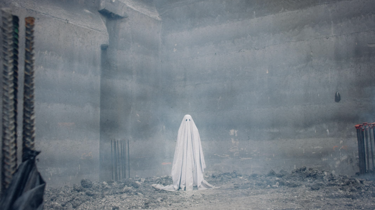 A ghostly figure in a white sheet stands amid a foggy, industrial construction site, with concrete walls and scattered debris.