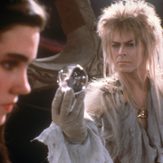 A character with flowing hair holds a crystal ball, surrounded by a mystical setting with rocks and shadows.