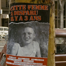 A missing person poster on a tree trunk, featuring a blurred image and text in French about a woman who disappeared three years ago.