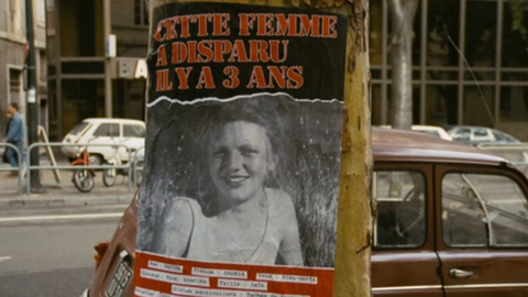 A missing person poster on a tree trunk, featuring a blurred image and text in French about a woman who disappeared three years ago.